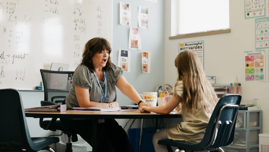 A Monument Academy teacher works one-on-one with an elementary student at a classroom table